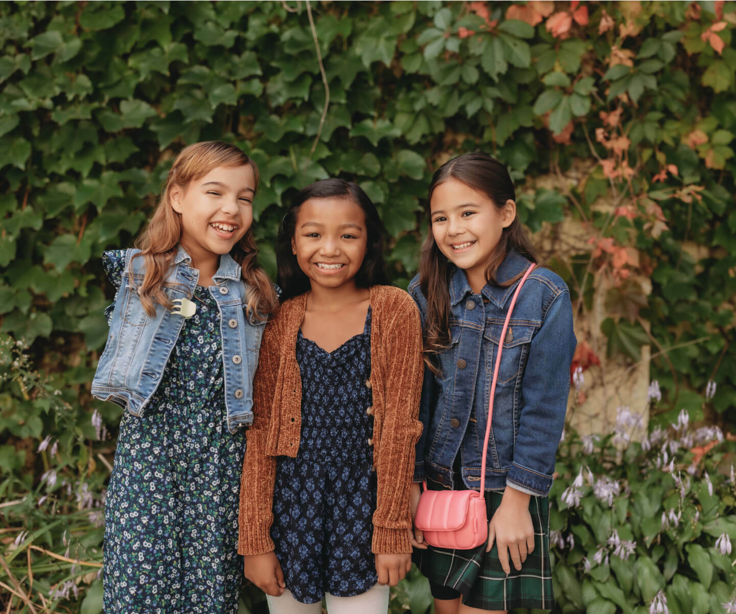 Three girls smiling and posing for a photo in front of a lush green bush